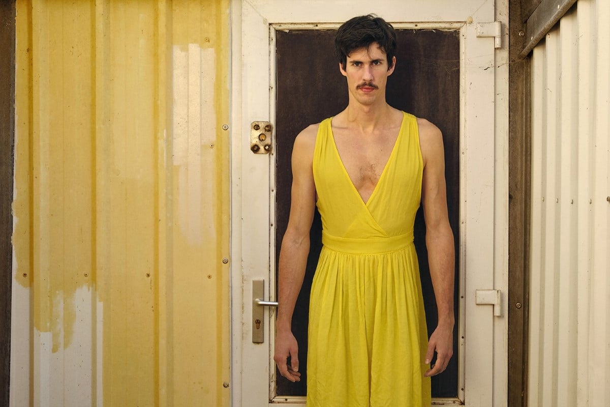Man wearing a yellow dress standing in front of a house