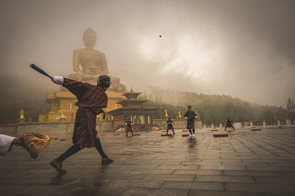 Teenagers in Bhutan playing baseball in front of a Buddha statue